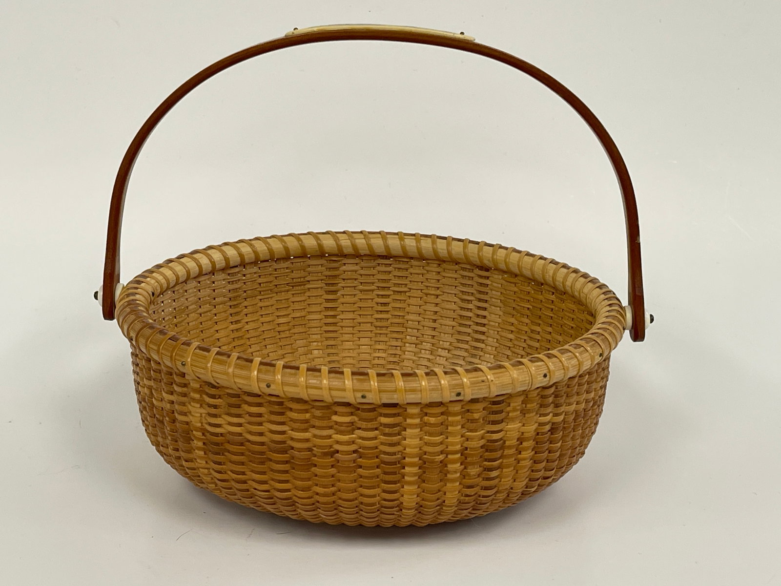 SHALLOW BASKET WITH SWING HANDLE BY MARTHA WETHERBEE: SHALLOW BASKET WITH SWING HANDLE BY MARTHA WETHERBEE, NEW HAMPSHIRE, 2005. WITH SCRIMSHAW PLAQUE OF SAILING SHIPS AND LIGHTHOUSE. INSCRIBED ON BOTTOM "MARTHA WETHERBEE 2005." MARTHA WETHERBEE COLLECTI
