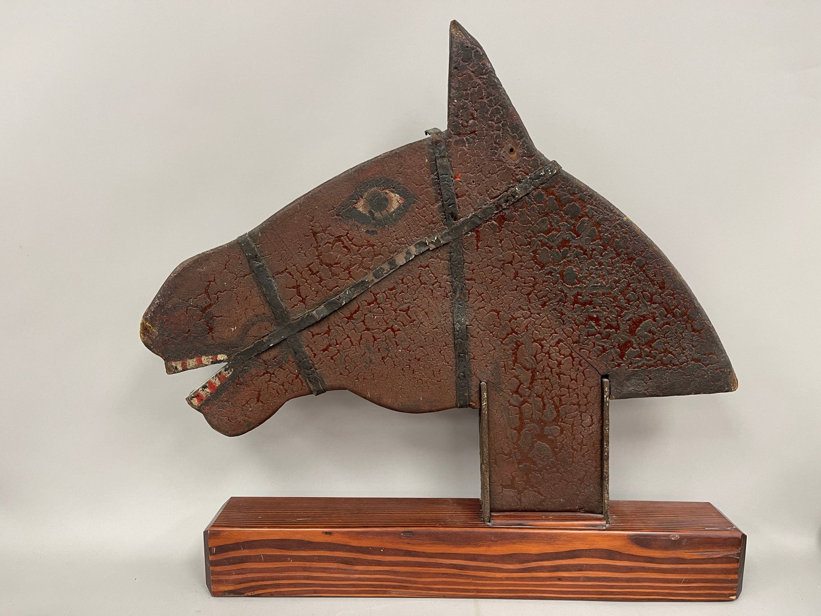 HORSE HEAD TRADE SIGN: HORSE HEAD TRADE SIGN C 1900, PINE, ORIGINAL CRUSTY BROWN PAINT WITH APPLIED METAL HARNESS, FLAT PROFILE CARVED, MODERN STAND, EXCELLENT CONDITION.