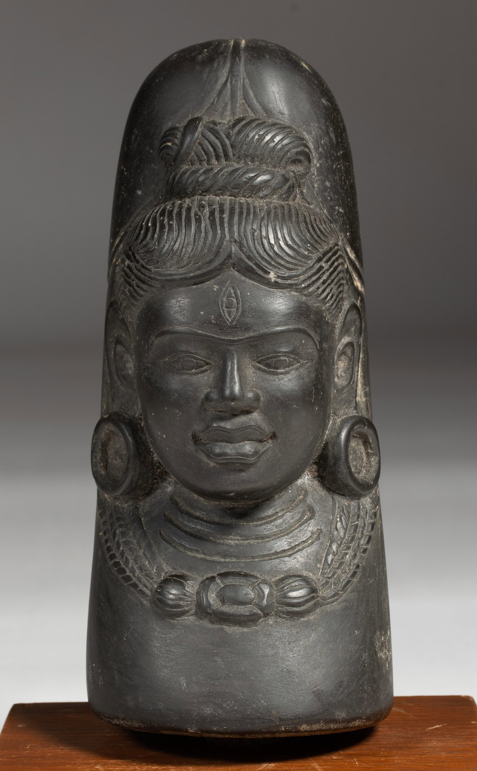 Carved Stone Linga with Face of Shiva - India: Ekmukha Shiva Linga (linga with one face). India. Age unknown. Carved black stone linga decorated with the face of Shiva. Unfinished protrusion on the bottom. Presently mounted / inserted into a moder