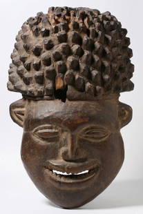 An Old African Helmut Mask - Bamileke Bamum: Carved and inlaid wood figure. Huari / Wari Culture. North Coast of Peru, circa 500 - 1000 AD. In the form of a crouching figure wearing a headdress, raised on a platform and holding two spears. Carve