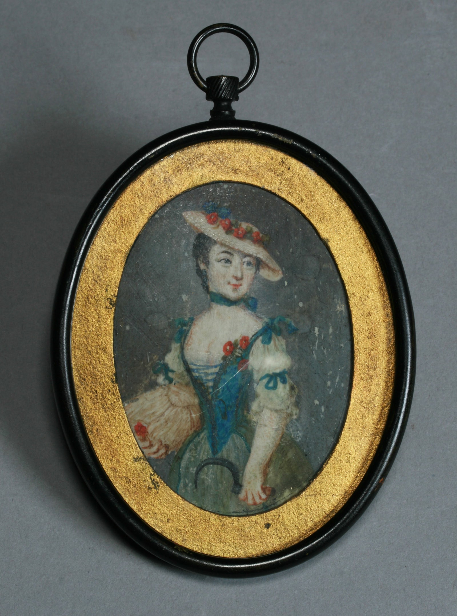 French Miniature Painting of a Country Farm Woman - 19th Century: An unusual 19th century French miniature painting depicting a smiling young woman in her finest country style dress, holding a scythe and a rose. Beautifully painted and mounted in an oval metal frame