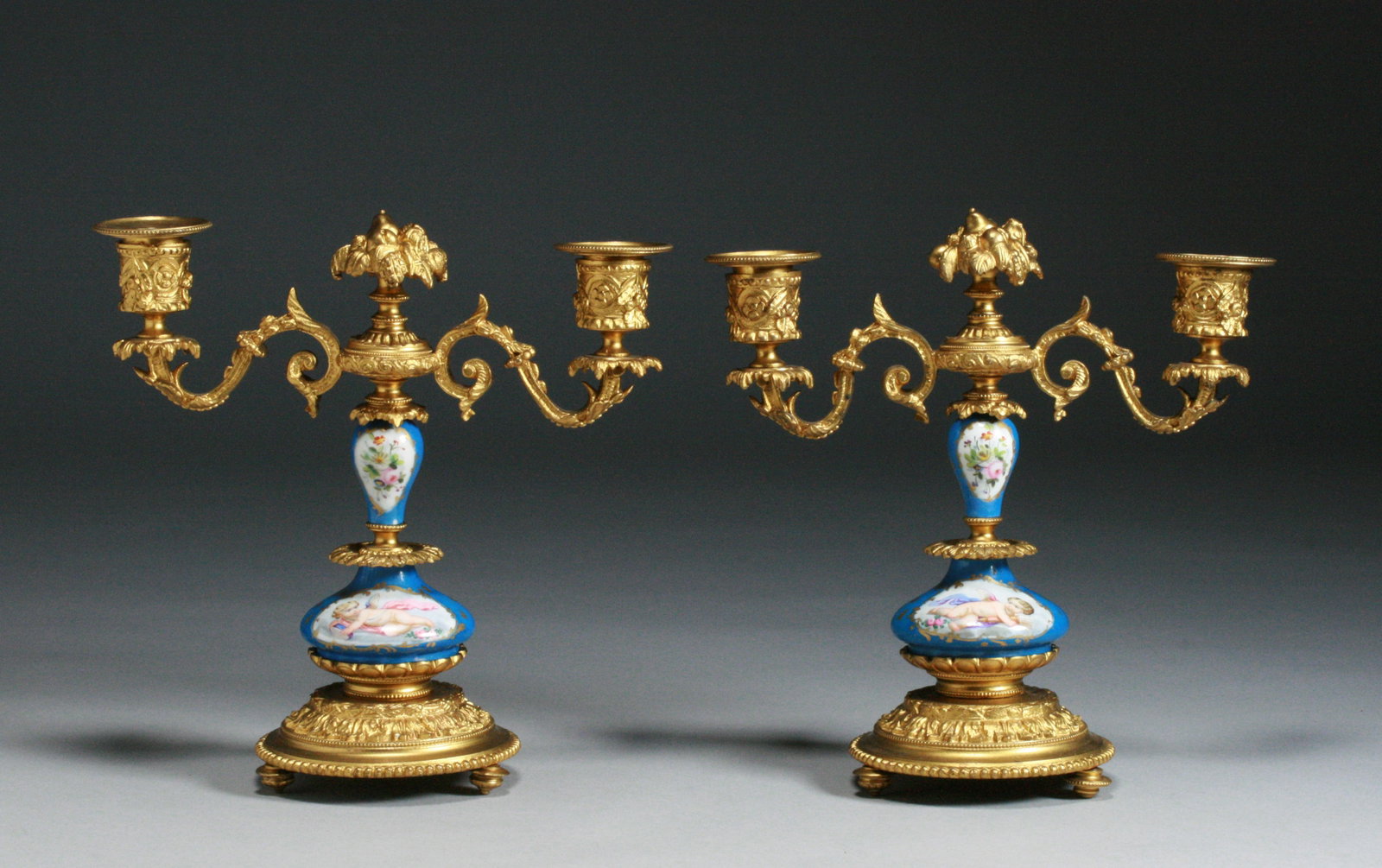Pair of French Sevres Porcelain & Ormolu Gilt Bronze Candlesticks: A very fine pair of French porcelain and gilt bronze candlesticks. Serves - 19th Century. Beautifully decorated with opposing Cherubs or Angels on the fronts and floral bouquet still lives on the back