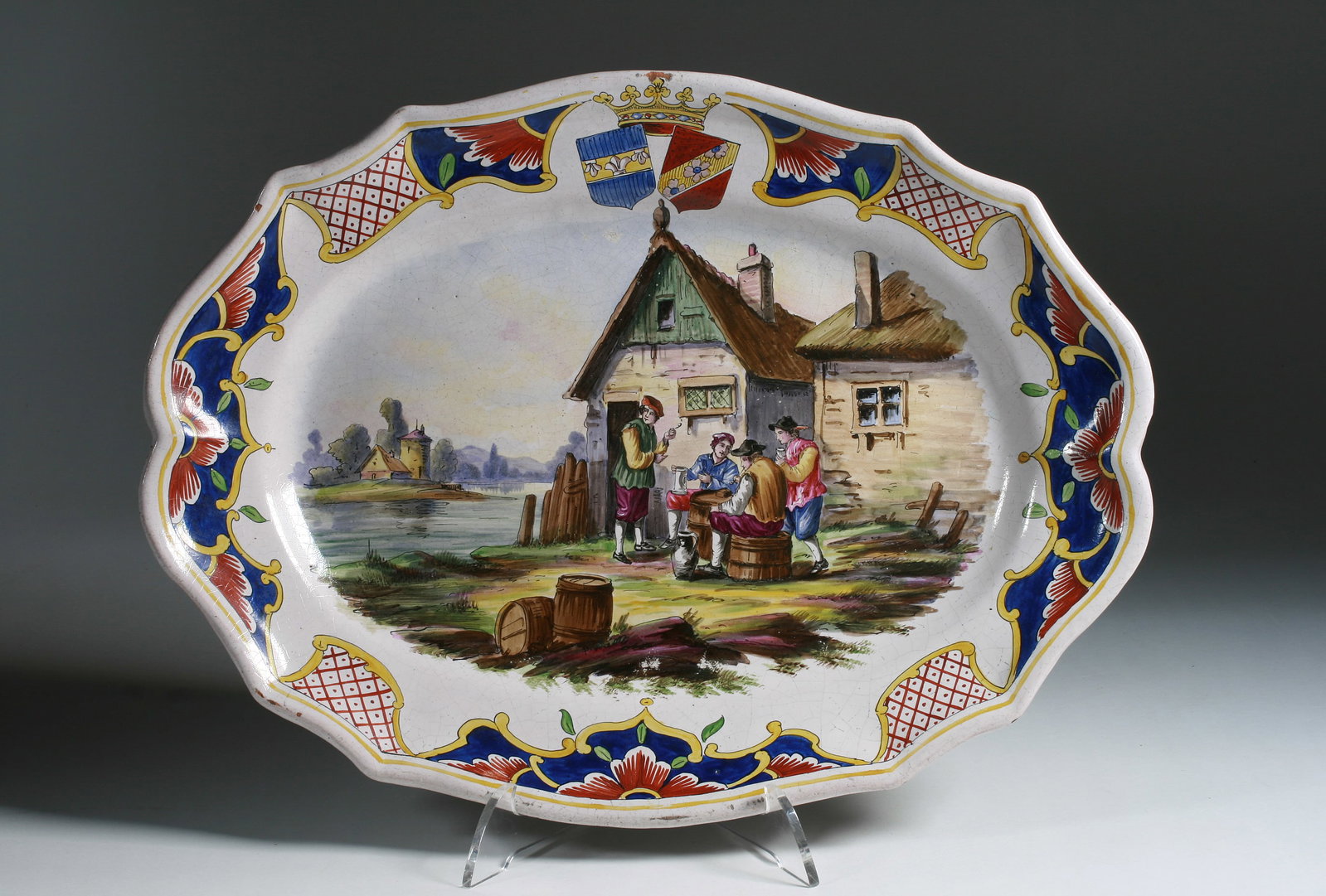 Large Faience Scenic Pottery Charger - French 19th Century: French faience hand-painted ceramic charger decorated with an extensive scene of men gathering in a village landscape. Borders painted with geometric floral designs and a crown with shields. Malicorne