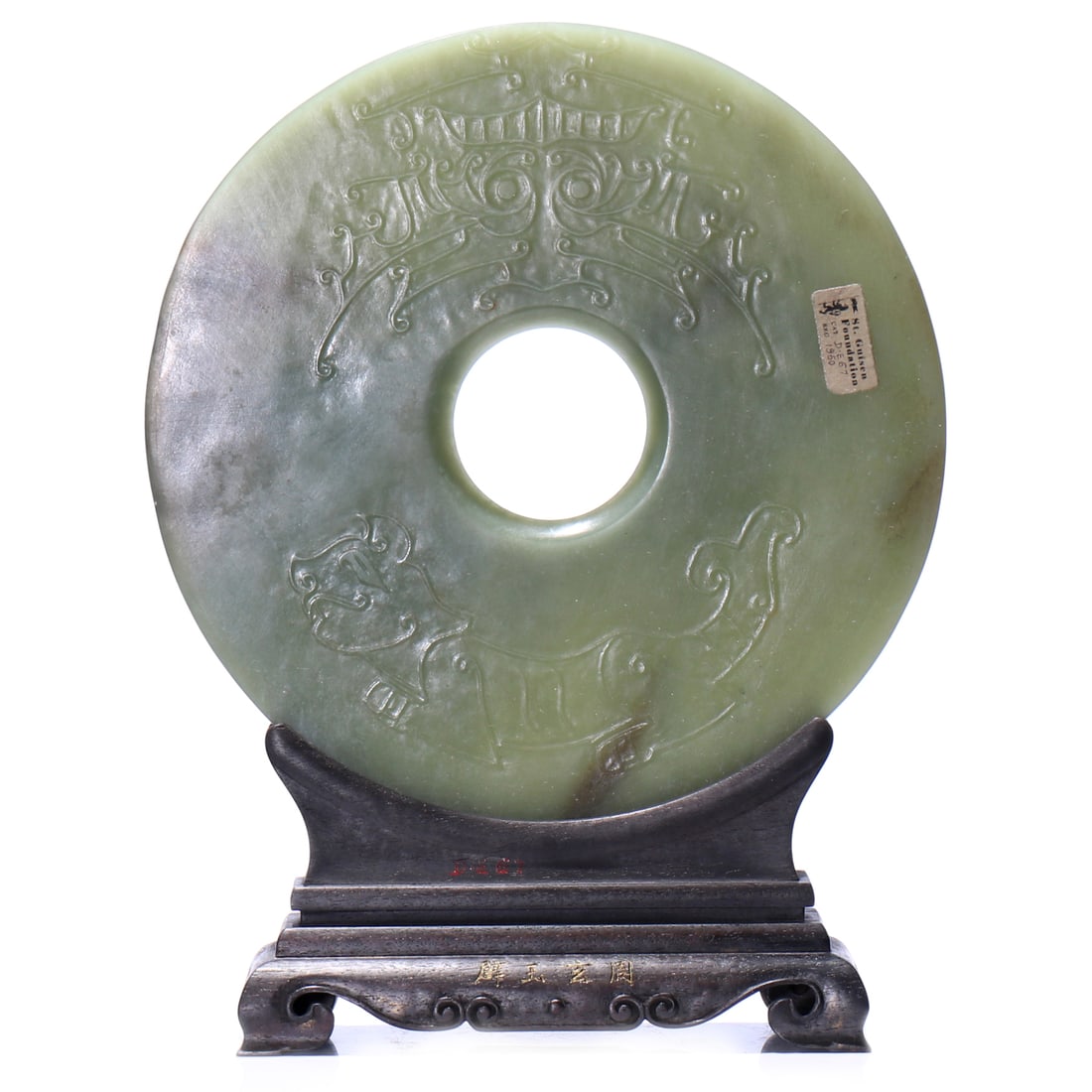 A Chinese Celdon Jade Carved 'Bi' With Stand: D 18.5 cm, height including accessories 23.5 cm.