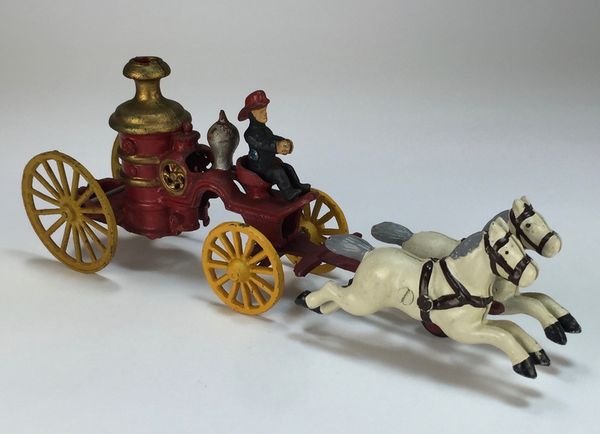Vintage Cast Iron Two-Horse Toy Fire-Pump Wagon: This vintage toy is in great shape, its white horses a-galloping to the fire at the urging of its driver. Paint has held up well, down to the driverâ€™s face and hands. 13â€ long and 4â€ hi