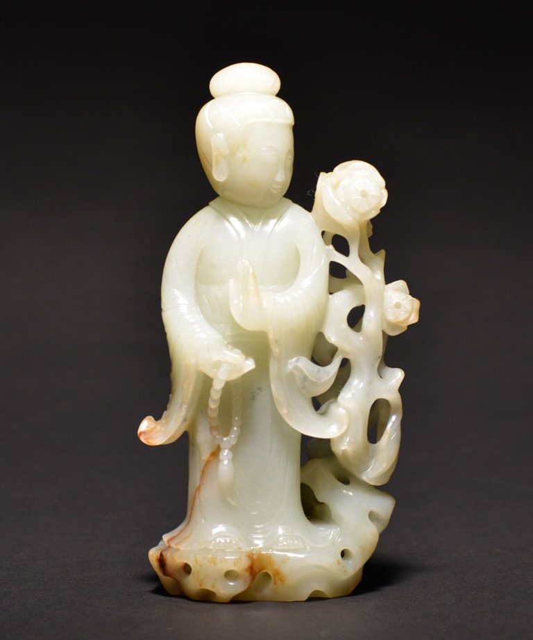A WHITE JADE CARVING OF BEAUTY: The carving is of an erected beauty wearing traditional robes and next to a flower blossom. Period: Qing Dynasty Size: 6 3/16 in. (15.7 cm) tall.