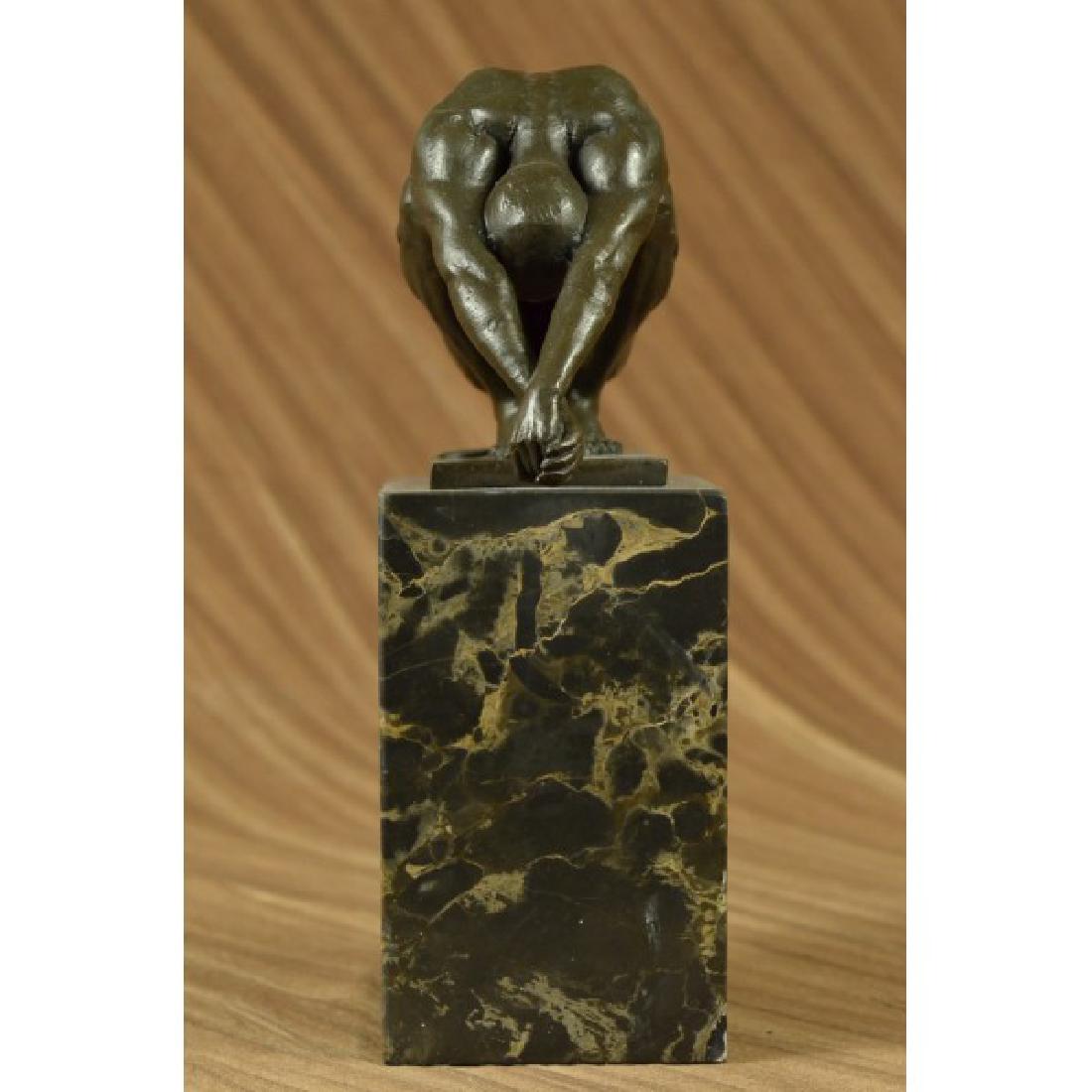 Nude Male Erotic Athletic Sensual Elegant Bronze Marble: This statue is a conceptual representation of a nude man sitting on top of a platform. He situated with both arms stretched while he leans forward and looks straight downward. He is clearly deep in th