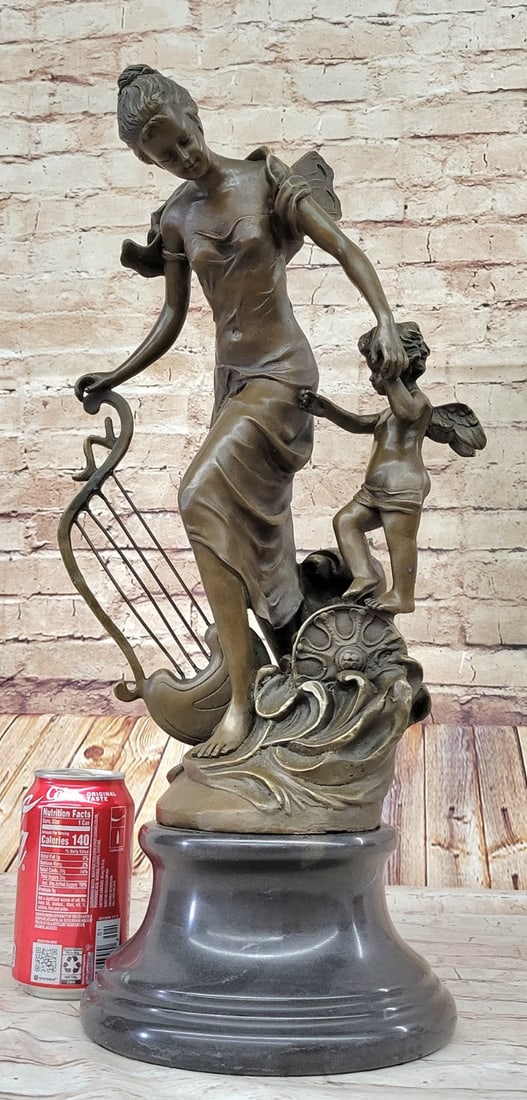 Fantasy Winged Fairy with Mythical Bronze Sculpture: A young cherub reaches to a fairy to gain her attention. The beautiful fairy reaches back to the cherub with a delicate to his playful curls. She\'92s holding a musical Harps in this enchanting sculpt