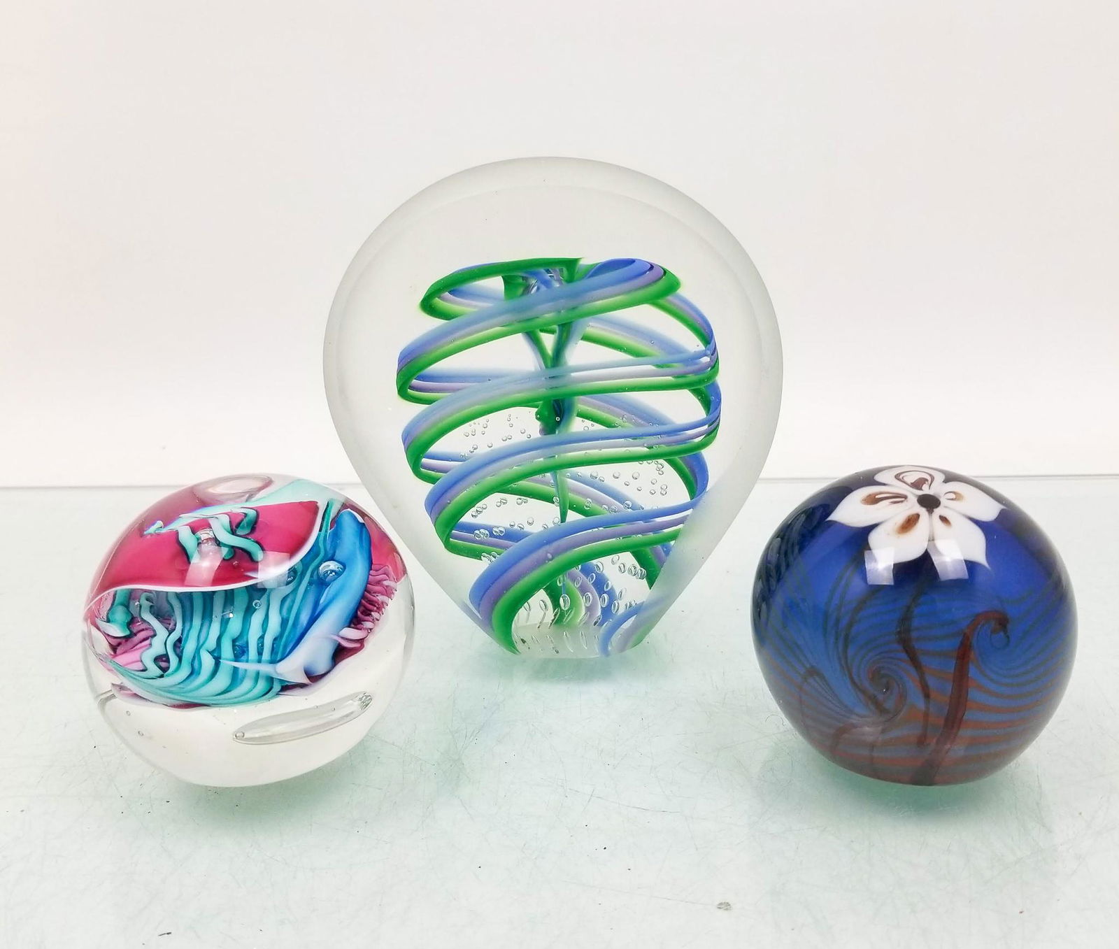 Three Art Glass Paperweights: (3) Art Glass Paperweights: blue and white floral, signed AGAG 1977 - multi color abstract, signed - standing blue and green frosted Literature Brooks Auction is not responsible for outbids. Question