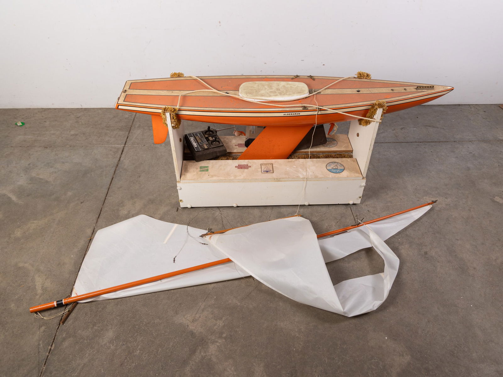 "Aldeberan" Vintage Remote Control Model Sailboat: "Aldeberan" Vintage Remote Control Model Sailboat: Needs some restoration, missing a motor and has some damage in some places. Includes stand, assorted parts, and remote control.Size50"