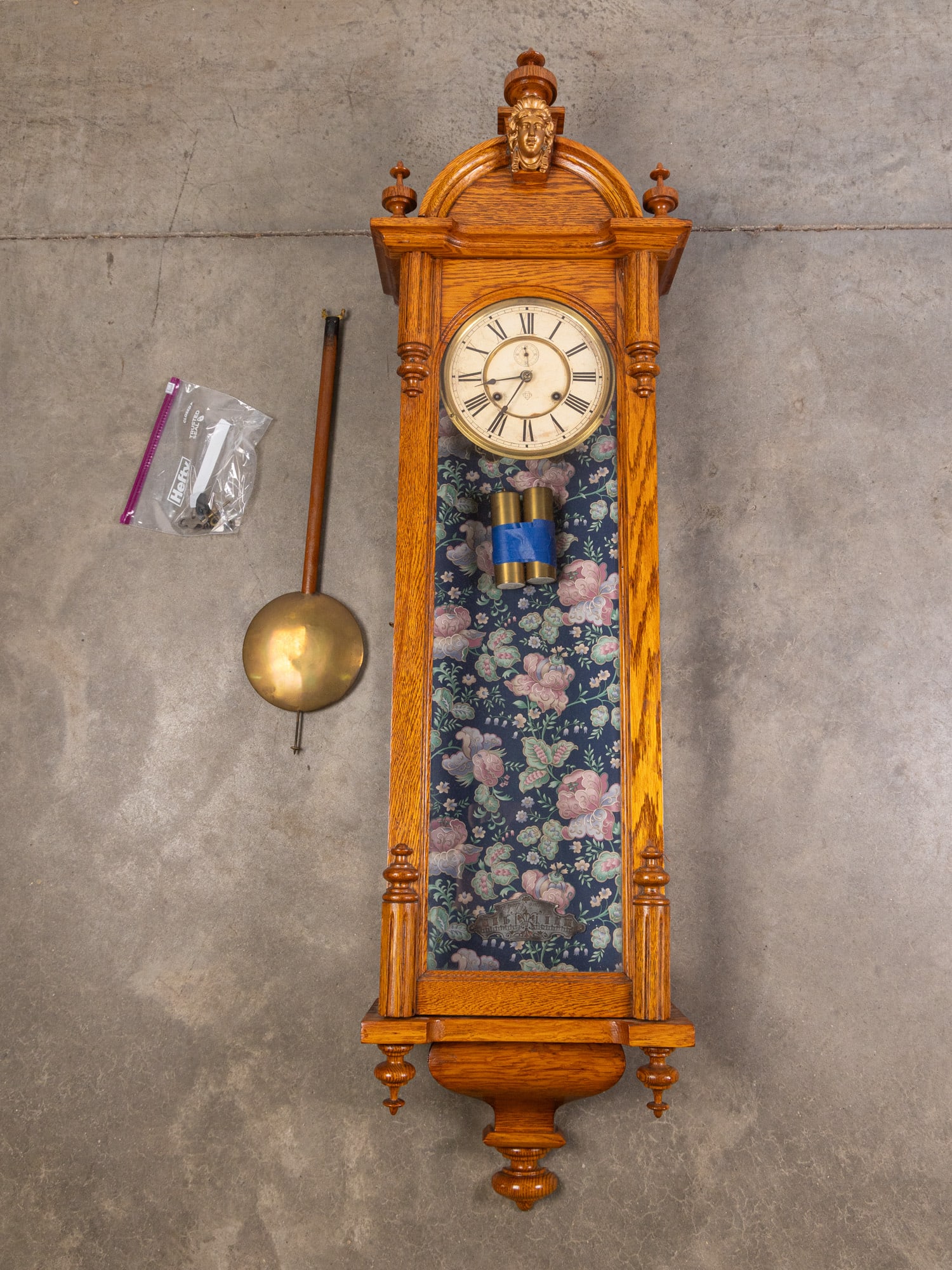 Ansonia "Capitol" Oak Wall Mounted Clock: Ansonia "Capitol" Oak Wall Mounted Clock, Gorgeous wall mounted clock with oak casing, paper on metal dial, and cameo detail. Decorative floral backing added at some point. Size 55" x 15" x 7" Literat