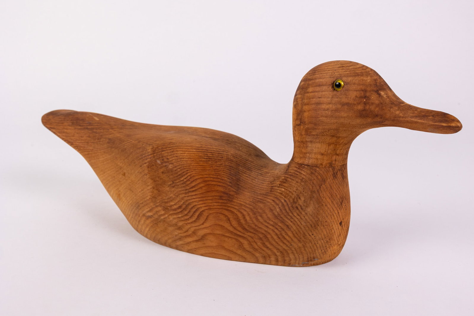 Vintage Hand Carved Duck Decoy w/ Natural Wood Grain: Crafted from solid wood, with a smooth stained finish & inset glass eyes. Size 7" x 4" x 16" Literature Brooks Auction – Online Auction Terms & Conditions Contact: (856) 694-2960 | info@brooks.