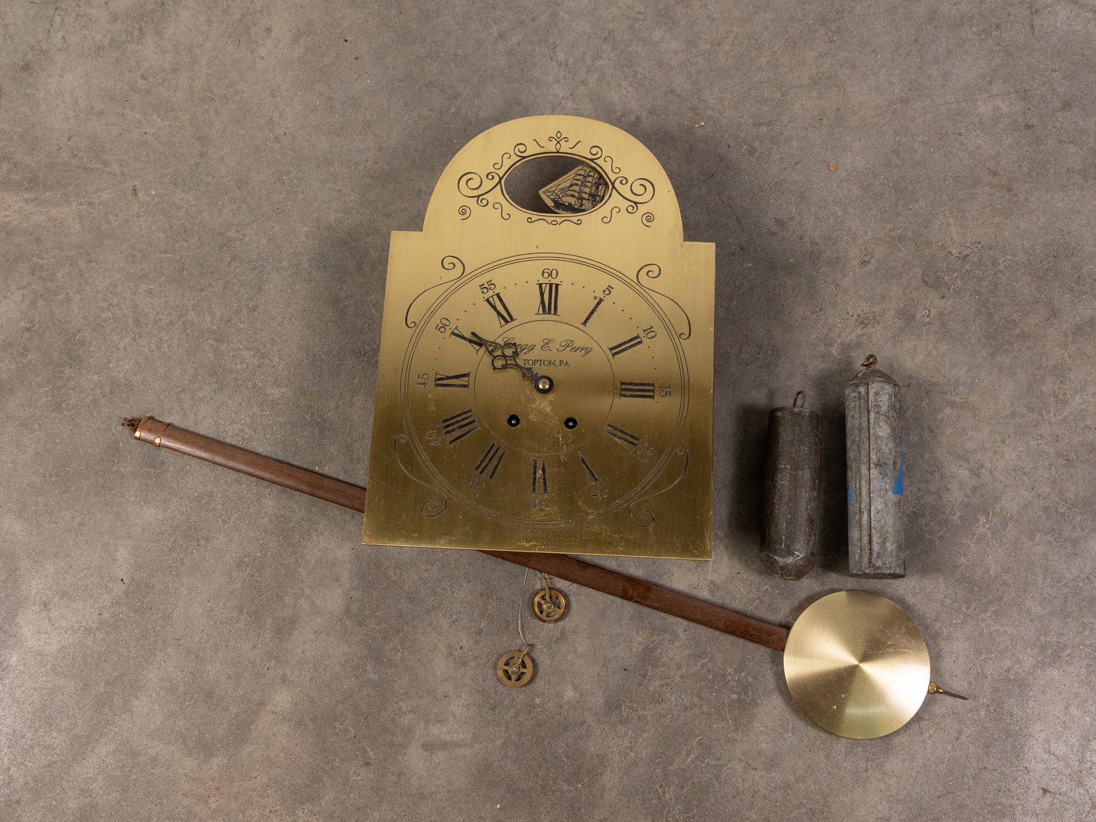 Gregg E. Perry Vintage Brass Clock Movement: Vintage brass clock movement signed Gregg E. Perry of Topton, PA. Etched Roman numerals and swirling design with rocking tall ship figure. Includes weights and pendulum. Size 15" x 10" Literature