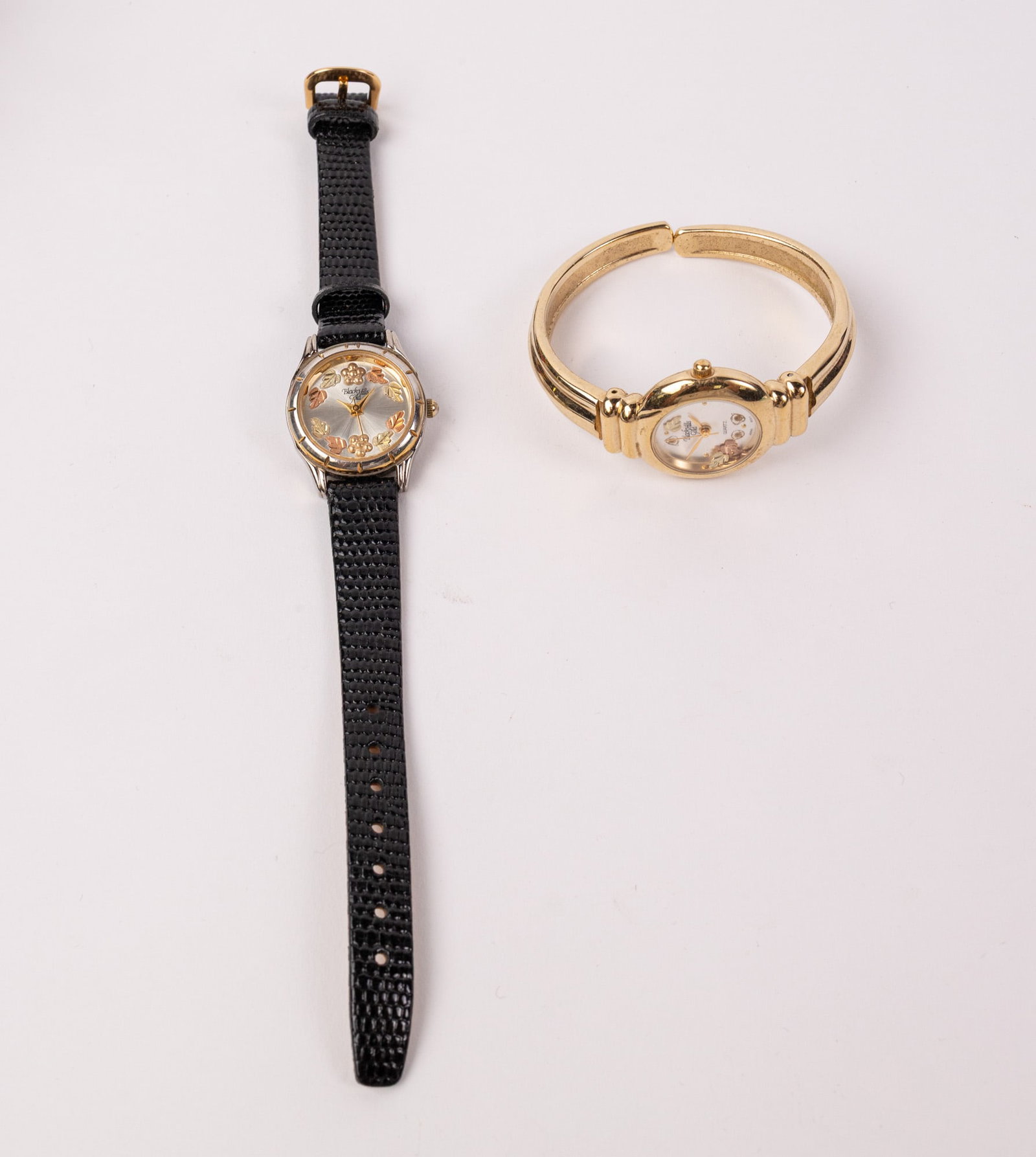 Pair of Black Hills Wrist Watches ft. 12KY Gold Leaf Accent Watch: Marked "12K Gold Leaves Made in USA Stainless Steel Back" Literature Brooks Auction – Online Auction Terms & Conditions Contact: (856) 694-2960 | info@brooks.auction READ BEFORE YOU BID: We want