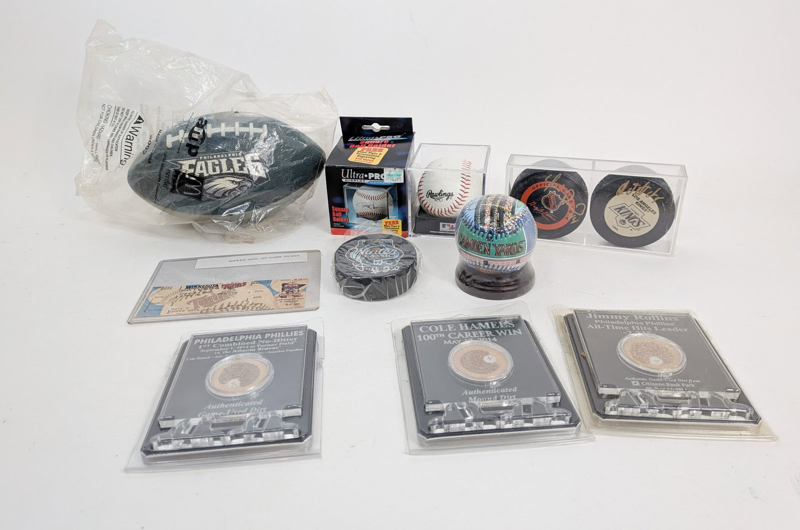 Assortment of Sports Memorabilia ft. Pucks with Signatures: This assortment lot of sports memorabilia features items such as yet-to-be-signed footballs, a novelty Camden Yards baseball, three hockey pucks with signatures such as Vitali Yachmenev, a game