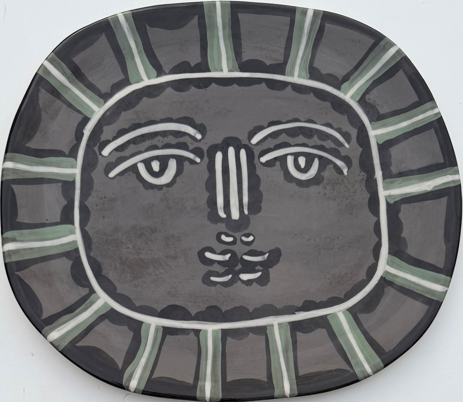 Pablo Picasso (In the Style Of), Ceramic Plate in the Style of Picasso. Magritte & Chagall Era: Title: Masked Face with Radiating Border? ?Technique: Ceramic Plate (Painted Glaze)? ?Measures: 13 × 14.5 inches? ?Year: Circa mid–20th century? ?Condition:?Good — the ceramic surface appears wel