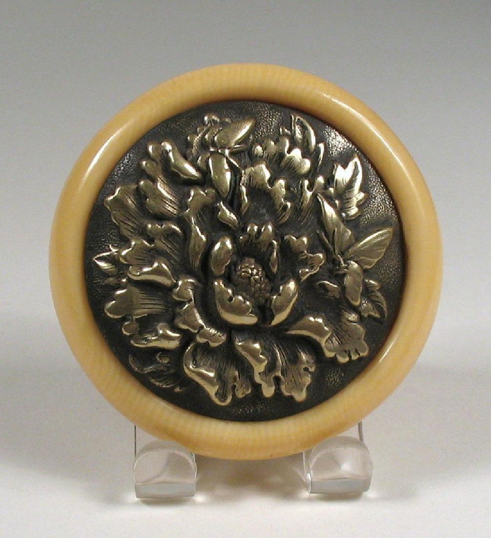 Japanese Kagamibuta Brass Netsuke, Late 19th C. Meji: A Japanese kagamibuta netsuke featuring a repossee brass chrysanthemum and butterfly in high relief, set in a round celluloid bowl. Originally attached to a purse or tobacco pouch by chain, holes have