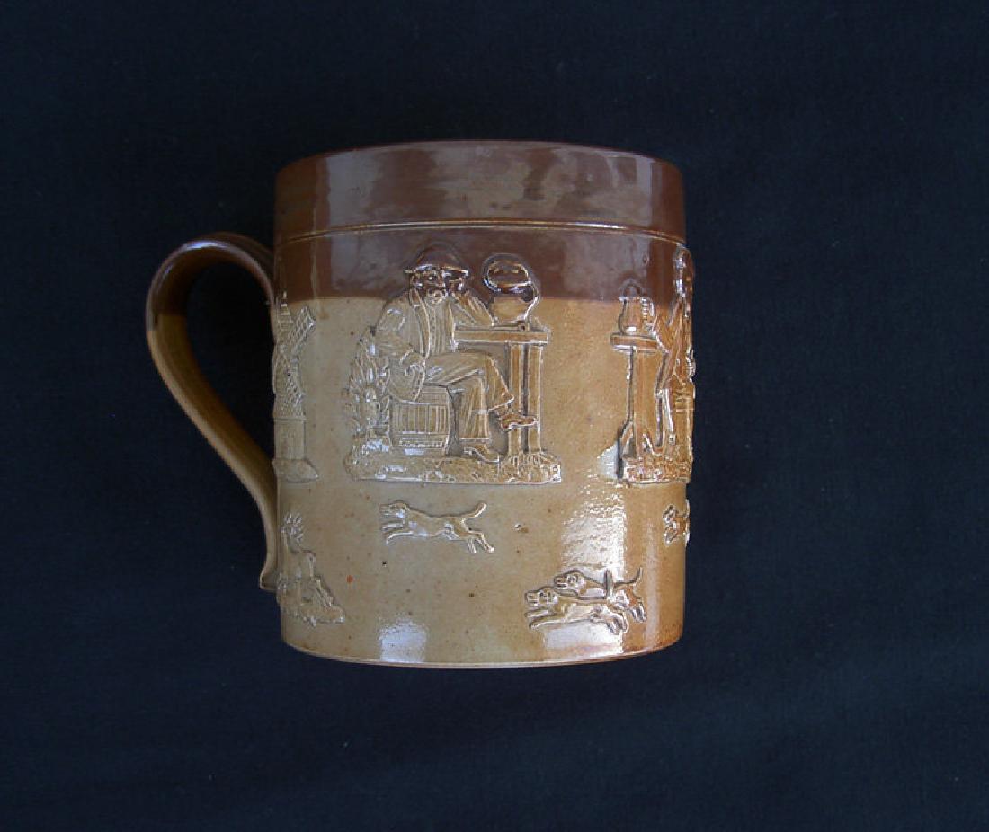 Doulton Lambeth Salt-Glazed Stoneware Victorian Tankard: A Doulton Lambeth stoneware tankard with applied decoration of naïve hunting, drinking and smoking scenes. Impressed mark for c 1869-72 and “ne”. Height: “4½ / 11 cm. Please note that this lot