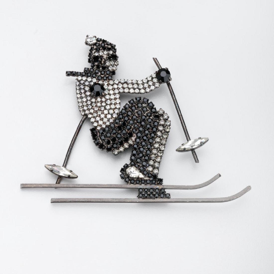 BUTLER & WILSON SKIER BROOCH: Butler & Wilson Skier Brooch. This figural brooch of a downhill skier. The brooch is set with clear and black faceted rhinestones set in silver toned metal. The brooch measures 3.5 inches high and app