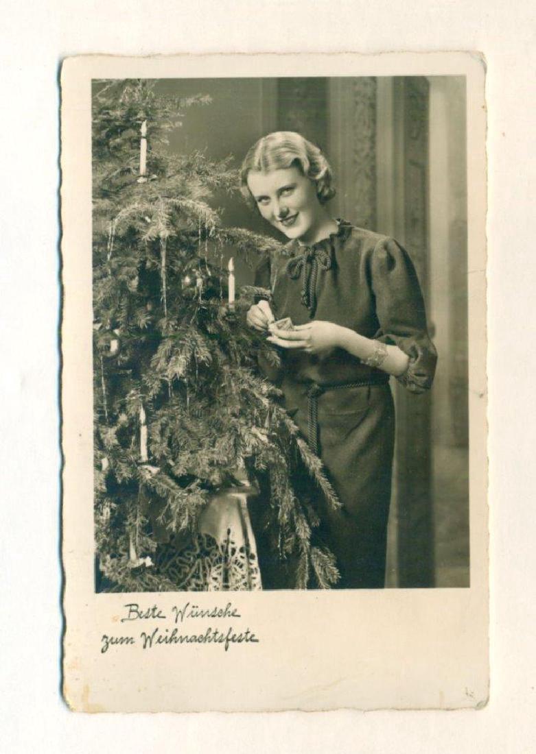 1939 WWII ERA ICONIC GERMAN CHRISTMAS POSTCARD NAZI: Circa 1939 WWII Era German Christmas Real Photograph Postcard depicting blond haired woman lighting candles on a fir tree. Includes Nazi German military postmark, "FELDPOST". Period ink manuscript mes