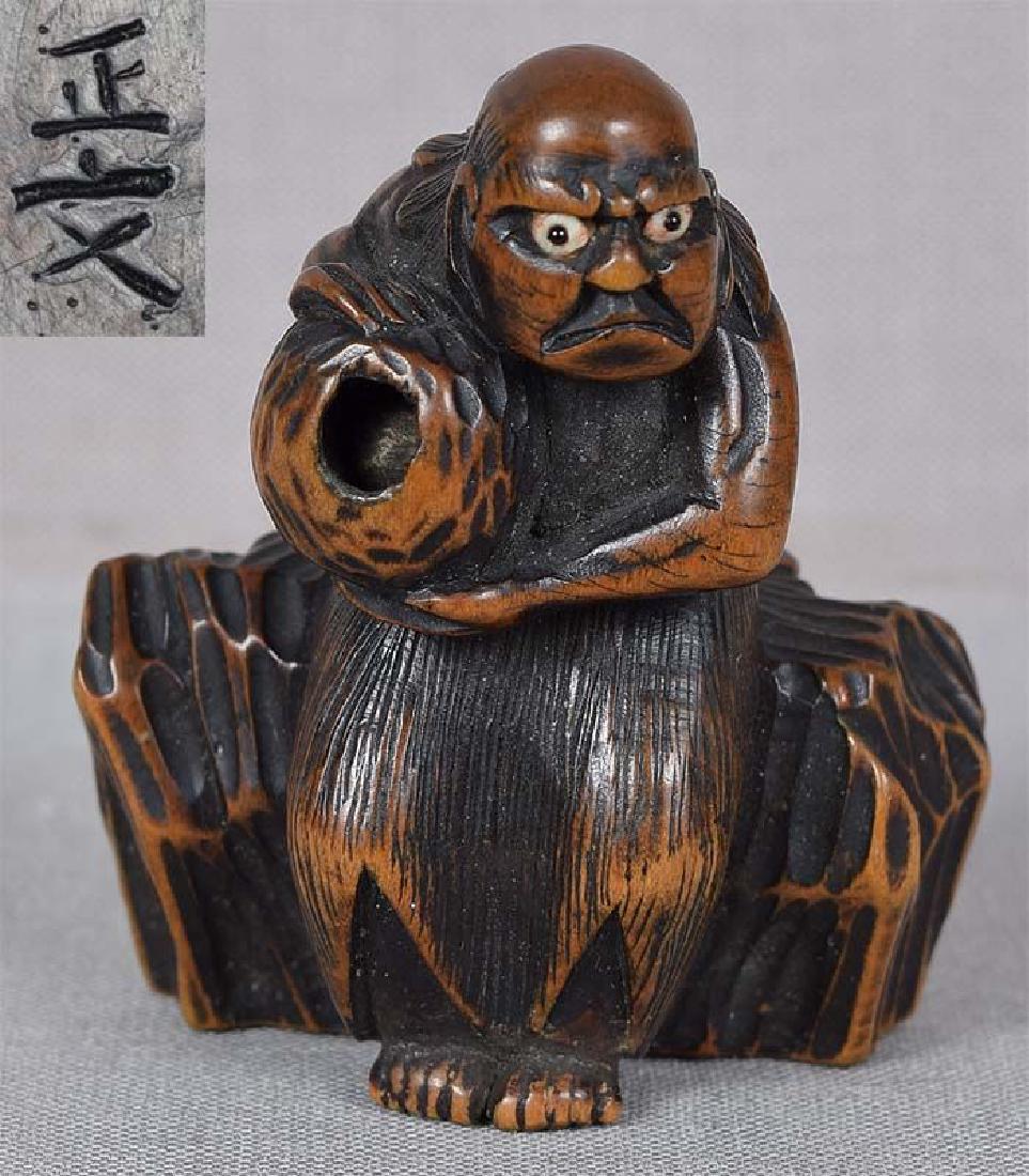 Antique Japanese Netsuke South Sea Islander by Masabumi: 19th century boxwood netsuke of a South Sea Islander wearing a straw skirt held by rope belt, seated on rockery and holding a large ball with an opening that contains a rolling ball inside it. Excelle