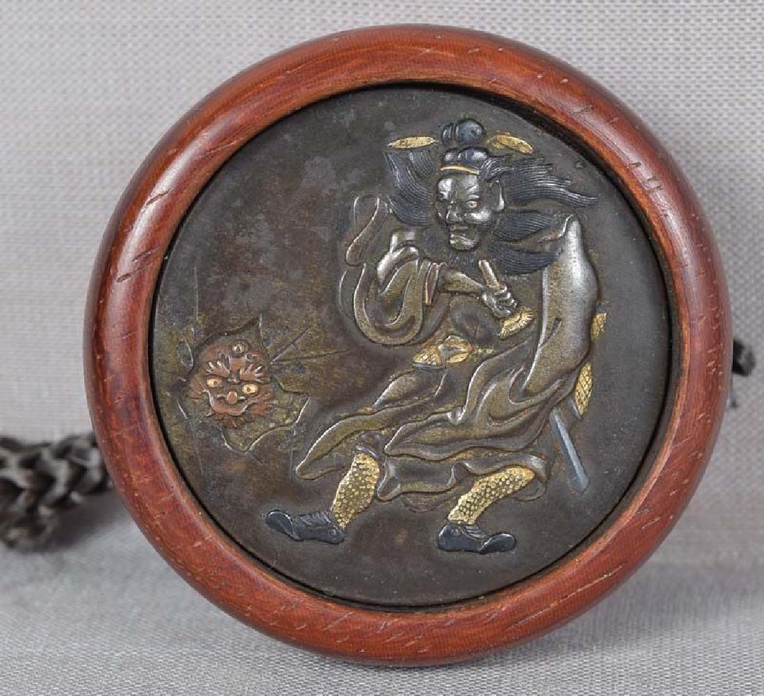 Antique Japanese Kagamibuta Netsuke Shoki & Oni: 19th century wood and metal kagamibuta (mirror lid) netsuke. Patinated bronze top with multimetal inlaid and carved design of Shoki the Demon Queller starting to draw a sword as he sees a demon coming