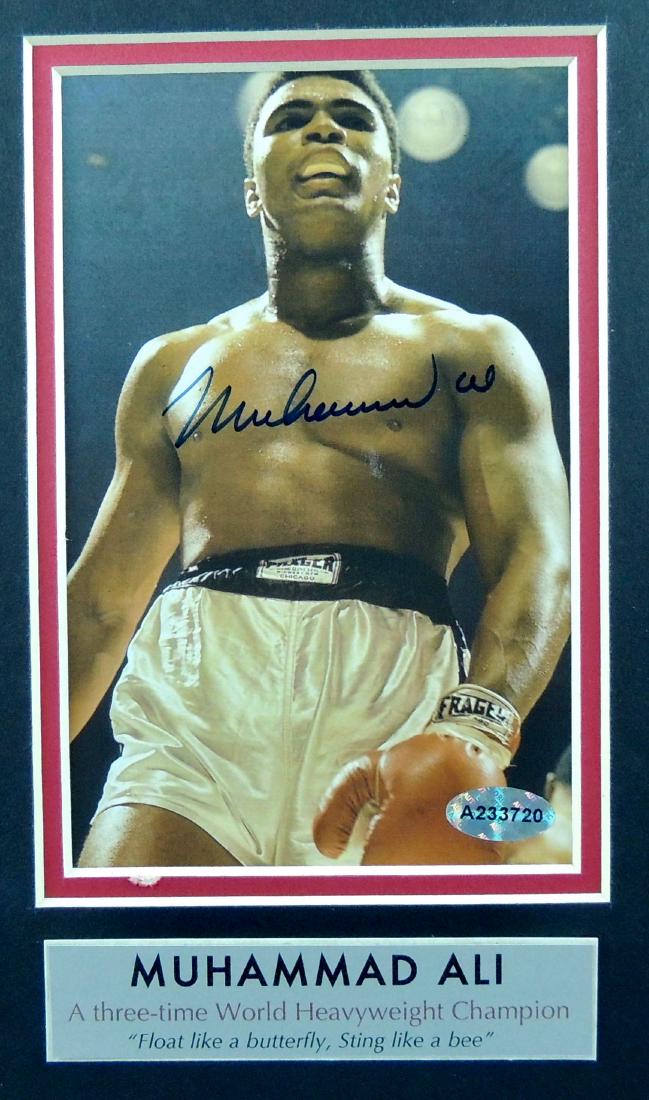 Muhammad Ali Signed FC Photo w/ COA: Muhammad Ali Signed FC Photo w/ COA. The 8” x 10” matted full color photo is signed in blue felt tip pen on Muhammad Ali’s chest area depicting a ring fight with below caption “Muhammad Ali, A