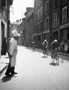 Chef Toasts Tour: Artist: Bert Hardy Title: Chef Toasts Tour Medium: Silver Gelatin Year: 1951 Height/Width: 16 x 12 in Description: A chef cheers on participants in the 1951 Tour de France as they speed past his resta