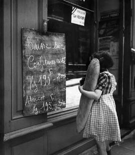 Girl And Baguette: Artist: Bert Hardy Title: Girl And Baguette Medium: Silver Gelatin Year: 1952 Height/Width: 16 x 12 in Description: A young girl holding a baguette as she reads a notice board displaying cuts in the