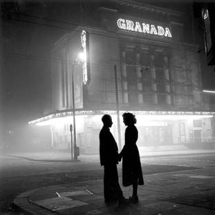 Off Duty Usherette: Artist: Bert Hardy Title: Off Duty Usherette Medium: Silver Gelatin Year: 1954 Height/Width: 30 x 30 in Description: circa 1954: A young woman talks to a boy friend after her evening’s work as a cin