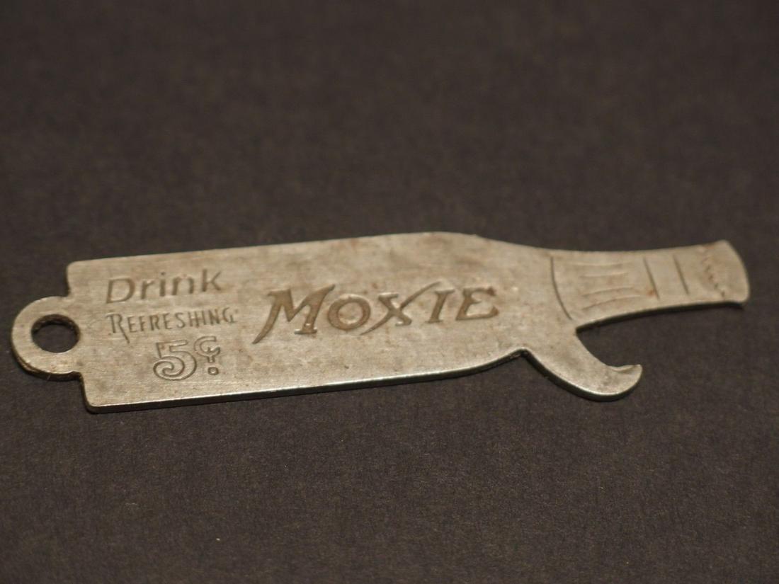 Moxie Bottle Cap Opener Lifter: 3 1/8" Long Nice reproduction Moxie bottle opener shaped like a bottle. It says Drink Refreshing Moxie on one side then "Purity is sealed in a bottle" The opener is an old silver pewter color likely s