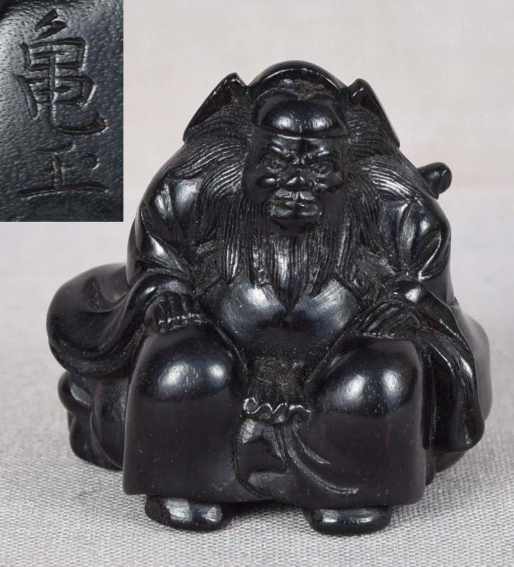 19c netsuke SHOKI with oni in bag by KIGYOKU: 19th century ebony netsuke of Shoki the Demon Queller seated on a bag containing a captured oni with its distressed face and one horn seen on the back and its claws ripping holes in the fabric on the 