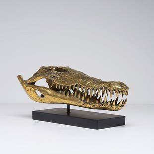 Saltwater Crocodile Skull in Polished Bronze: Title: Saltwater Crocodile Skull in Polished BronzeMaker: Designer: Jake RichmondOrigin: The NetherlandsDate/Period: 2018Materials:Bronze, WoodDimensions:DIMENSIONSLength: 42cmWidth: 20cmHeight: