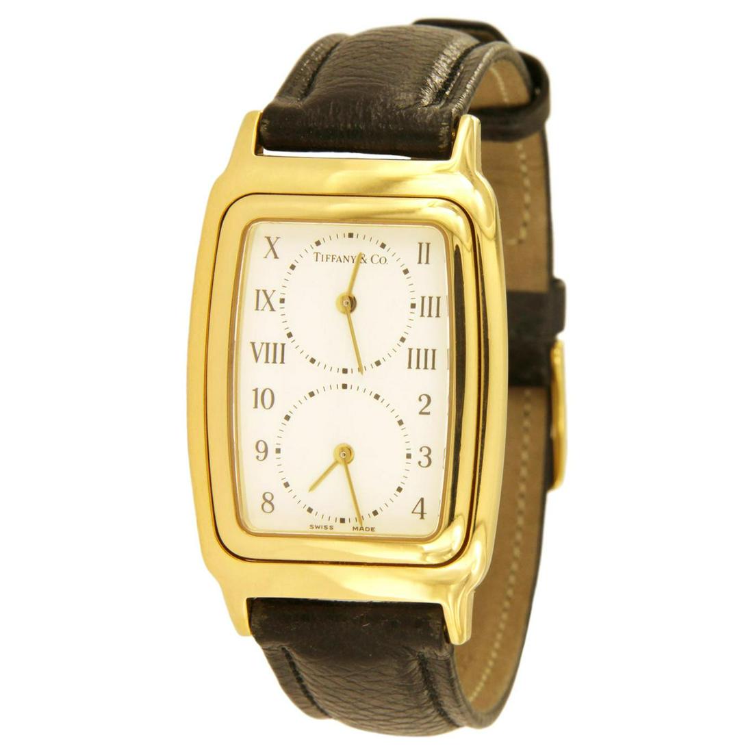 Tiffany & Co. 18 Karat Yellow Gold Dual Time Zone Watch: Case size: 26.5 mm Case thickness: 6.5mm Case: 18k Yellow Gold Movement: Swiss Quartz Dial: White with Roman Numerals and Arabic Numbers Strap: Black Leather Details Creator Tiffany & Co. Place of Ori