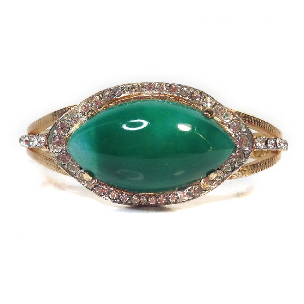 Clamping Cuff with Large Green Stone: Vintage costume jewelry from the 1960s Materials: Glass, Metal A gold tone metal box clasped hinged clamping cuff with a single large simulated jade glass stone framed by pavé set clear rhinestones.