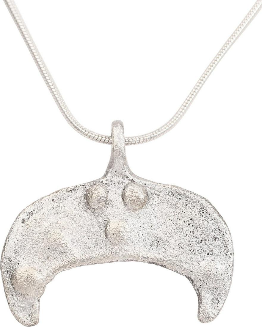 FINE VIKING LUNAR/ASTROLOGICAL PENDANT C.900-1050 AD.: Silvered bronze, over 1 1/8” width. Crescent form, of flat section, with low raised edge. Each tip with a circular mound, probably representing Sol the sun and Mani the moon. An additional cluster o