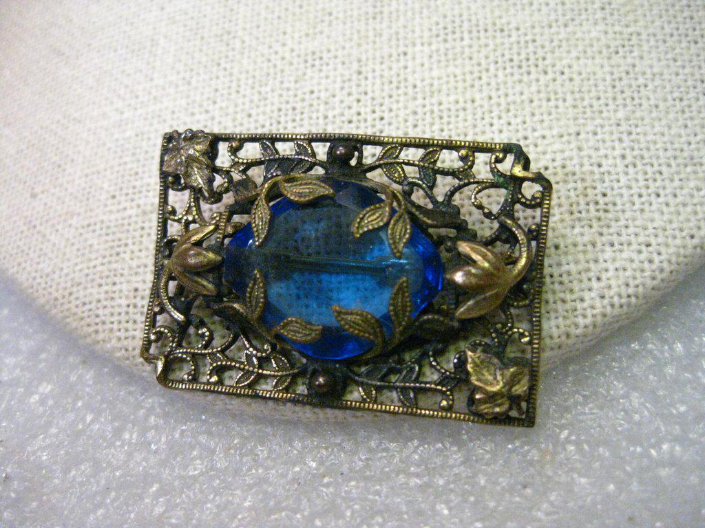 True Vintage late Victorian Brooch - it is a floral: True Vintage late Victorian Brooch - it is a floral filigree brassy gold tone rectangular brooch with a faceted blue stone that is held in place by vine-like trailing leaves that act as the prongs. Th