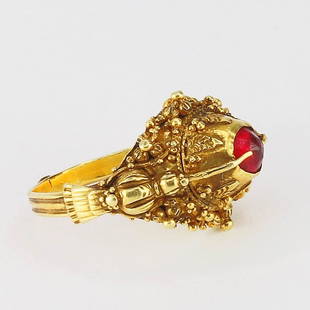 A GOLD AND RUBY RING: A GOLD AND RUBY RING; A granulated gold- heaped ring set with a single faceted ruby held in place with two claws. The shank is ribbed with a single motif in the middle of the shank. This type was