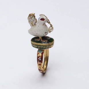 A Gold Bird Ring: A Gold Bird Ring; A gold ring depicting a bird with a Basra pearl hanging from its beak is enameled, the bird with white opaque enamel and red translucent eyes. The bird stands on a green enameled