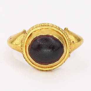 Garnet and Gold Ring: Garnet and Gold Ring; A small gold ring set with a large single tumbled garnet set within a high collar and a ring of granulation. The shoulders of which have small details to each side. Reserve: