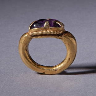 GOLD AND AMETHYST RING: GOLD AND AMETHYST RING; A gold ring with heavy shank rising to support a circular bezel which is bordered by a spiral wire filigree and which holds a cabochon amethyst by means of four triangles. 