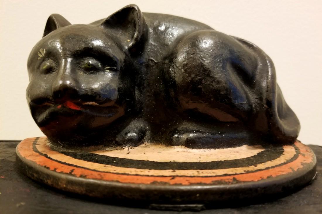 CUTE BLACK CAT RESTING ON A COLORFUL RUG: Title: CUTE BLACK CAT RESTING ON A COLORFUL RUG Date: 1920 Origin: ALBANY NY Material: CAST IRON Dimensions:73/8 X3 5/8 Provenance/additional info: ATTRIBUTED TO THE ALBANY FOUNDRY, NY. IN ORIGINAL PA