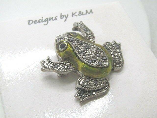 Green Enameled Faux Marcasite Frog Brooch by Designs by: Green Enameled Faux Marcasite Frog Brooch by Designs by K & M - it has an illusion design looking like marcasites - there are some smoky rhinestones too It is 1.25" tall and about 1.5" wide at the rea