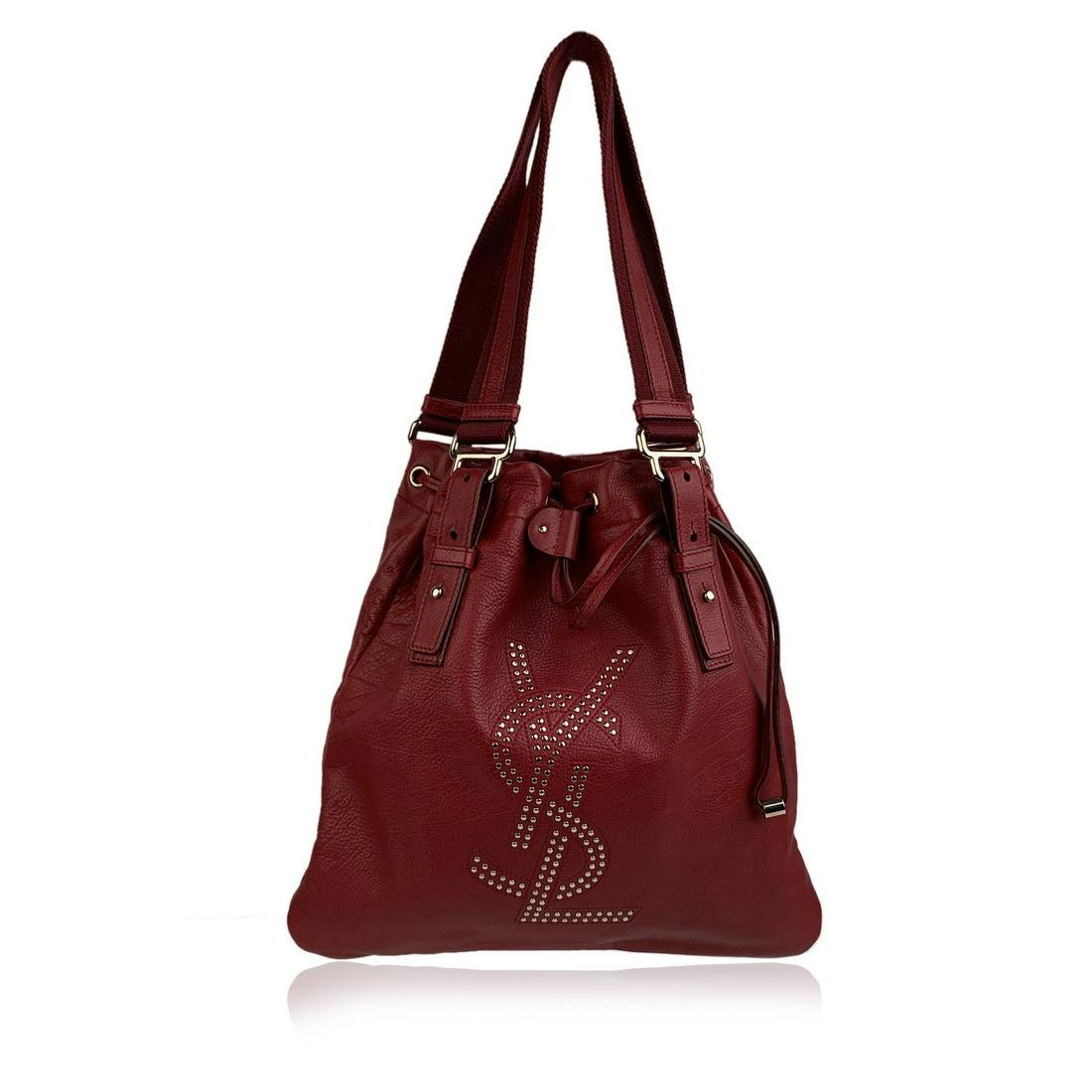 Yves Saint Laurent Red Leather Small Kahala Sac Tote: YVES SAINT LAURENT red leather 'Kahala Sac' tote bag with silver metal studded YSL logo on the front. Drawstring closure on top. Double canvas and leather handles/straps. Black satin lining. 1 side zi