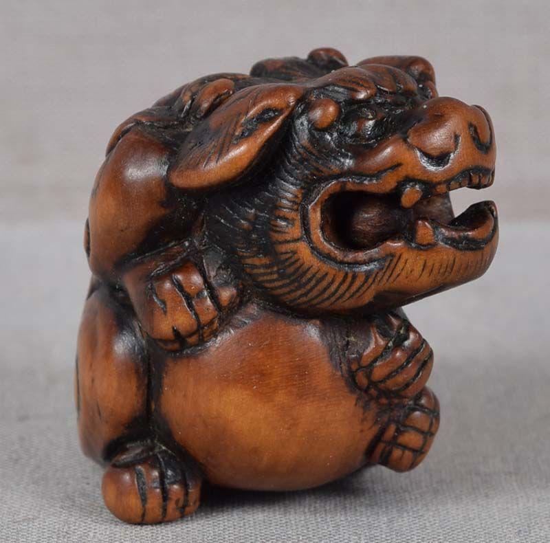 18c netsuke SHISHI with ball: Late 18th century boxwood netsuke of a shishi (Buddhist lion) seated with all of its paws hugging a large ball. Wonderful depiction of its ferocious face and curly mane, there is a loose ball in its m