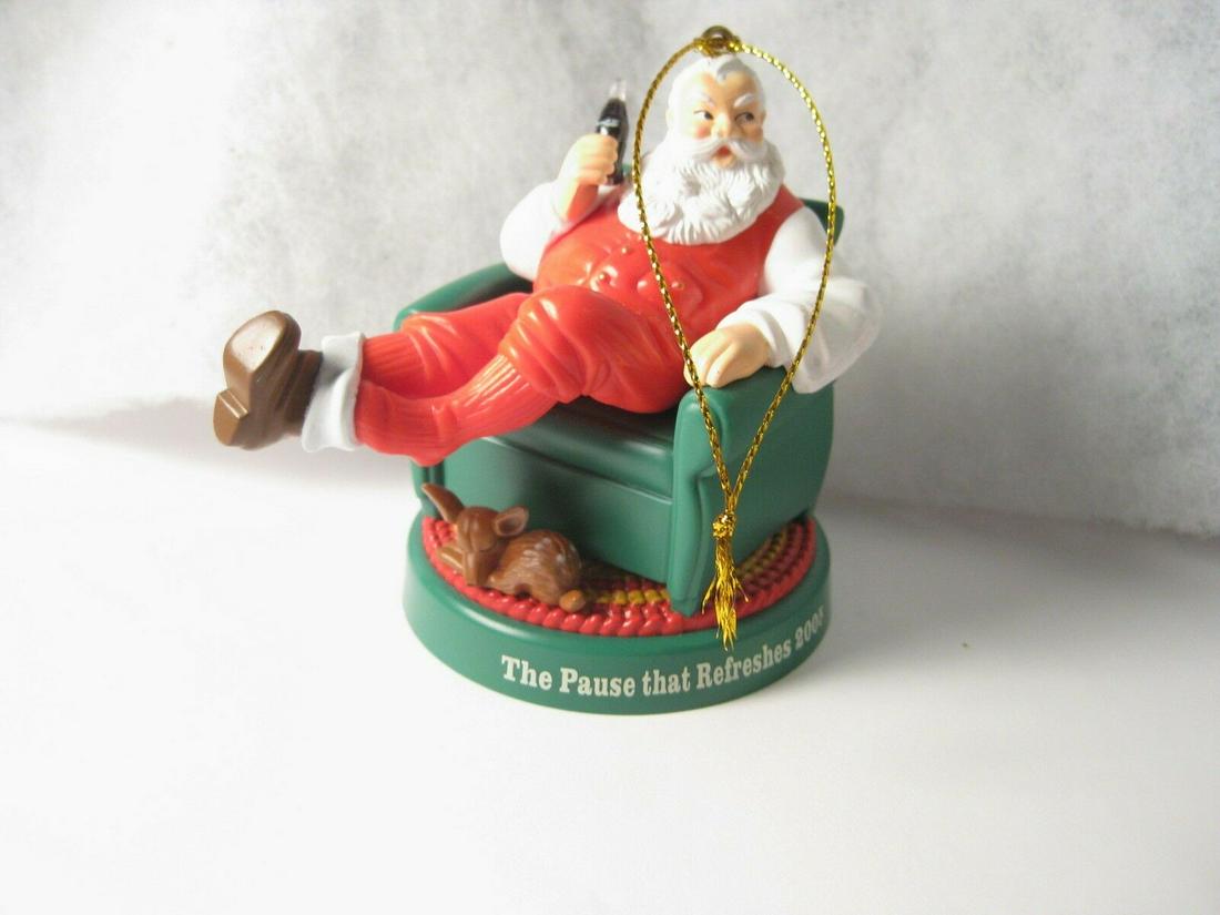 2005 Coca Cola Santa Ornament (sitting in chair with: 2005 Santa Claus Coca Cola Ornament - "The Pause That Refreshes" - Santa kicking off his boots having a coat, sitting in a green chair with a fawn curled up under his feet. It is about 3.25" tall and