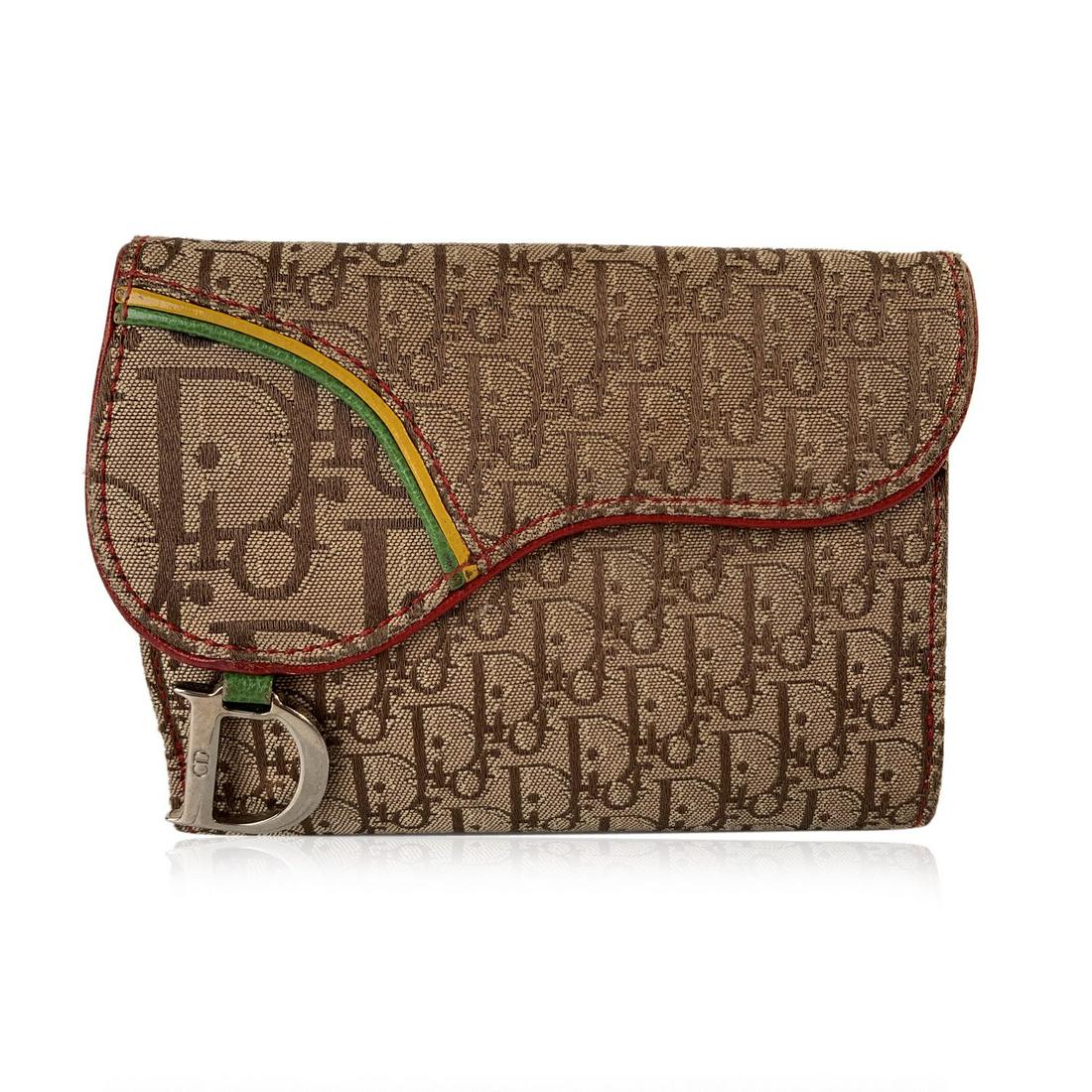 Christian Dior Beige Diorissimo Canvas Rasta Saddle: Christian Dior Rasta Saddle Wallet. Beige Diorissimo Canvas and Green Red Yellow genuine leather trim. D silver metal charm on the front. Brown leather interior. Flap coin compartment with snap button