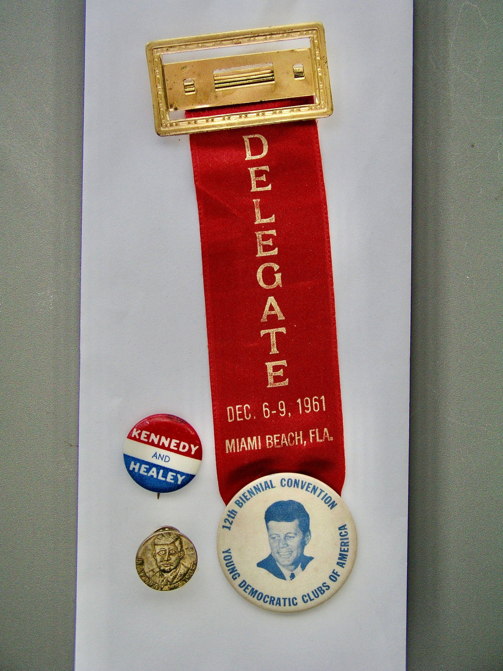 John F. Kennedy: Three Campaign or Election Badges: Title: John F. Kennedy: Three Campaign or Election Badges Origin: Dallas Provenance/Additional Info: Includes an 1” coattail button for “Kennedy and Healy”, a 3/4” brass portrait tie-tack capt