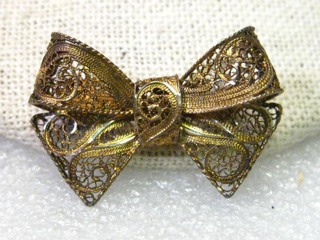 True Art Deco Filigree Bow Brooch, gold tone, 1.25": True Art Deco Gold Tone Filigree Bow Brooch. It has an upper loop and the tails below it. It is 1.25" wide and about 3/4" tall. It's weight for wearing purposes is appx. 4.38 grams. It Is true Art Dec