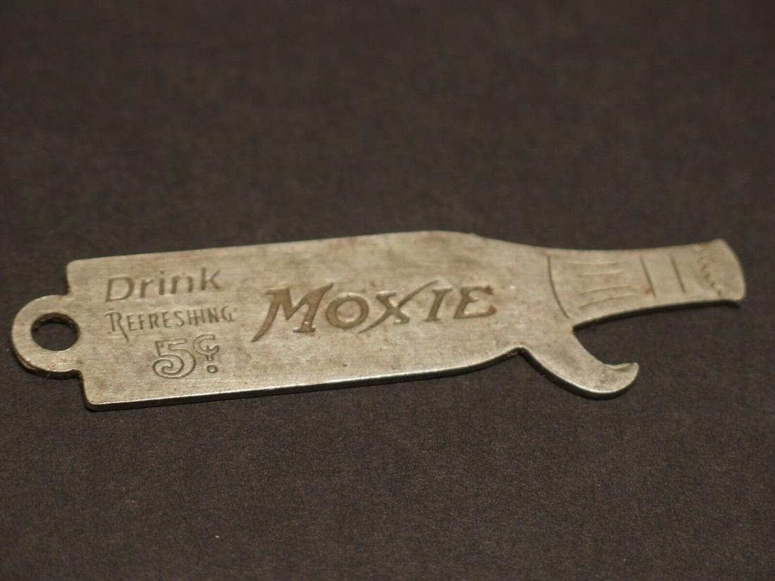 Moxie Bottle Cap Opener Lifter: 3 1/8" Long Nice reproduction Moxie bottle opener shaped like a bottle. It says Drink Refreshing Moxie on one side then "Purity is sealed in a bottle" The opener is an old silver pewter color likely s